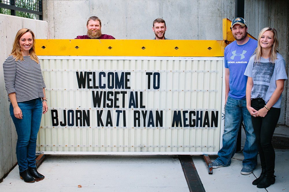 Wisetail employees Kati, Bjorn, Ryan, Kevin, and Meghan take a picture in front of the Wisetail marquee during their employee onboarding.