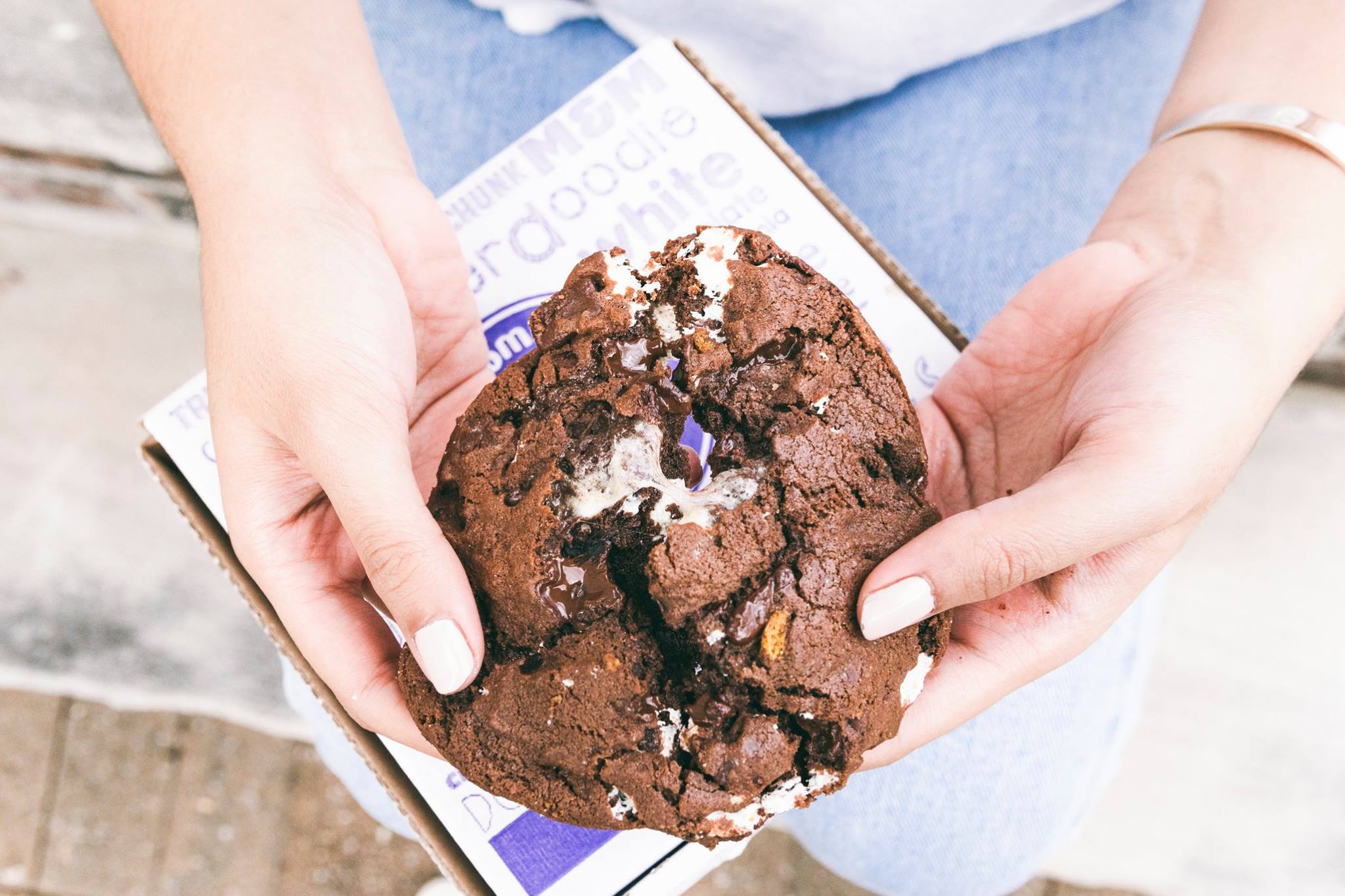 woman's hands pulling apart a gooey chocolate cookie