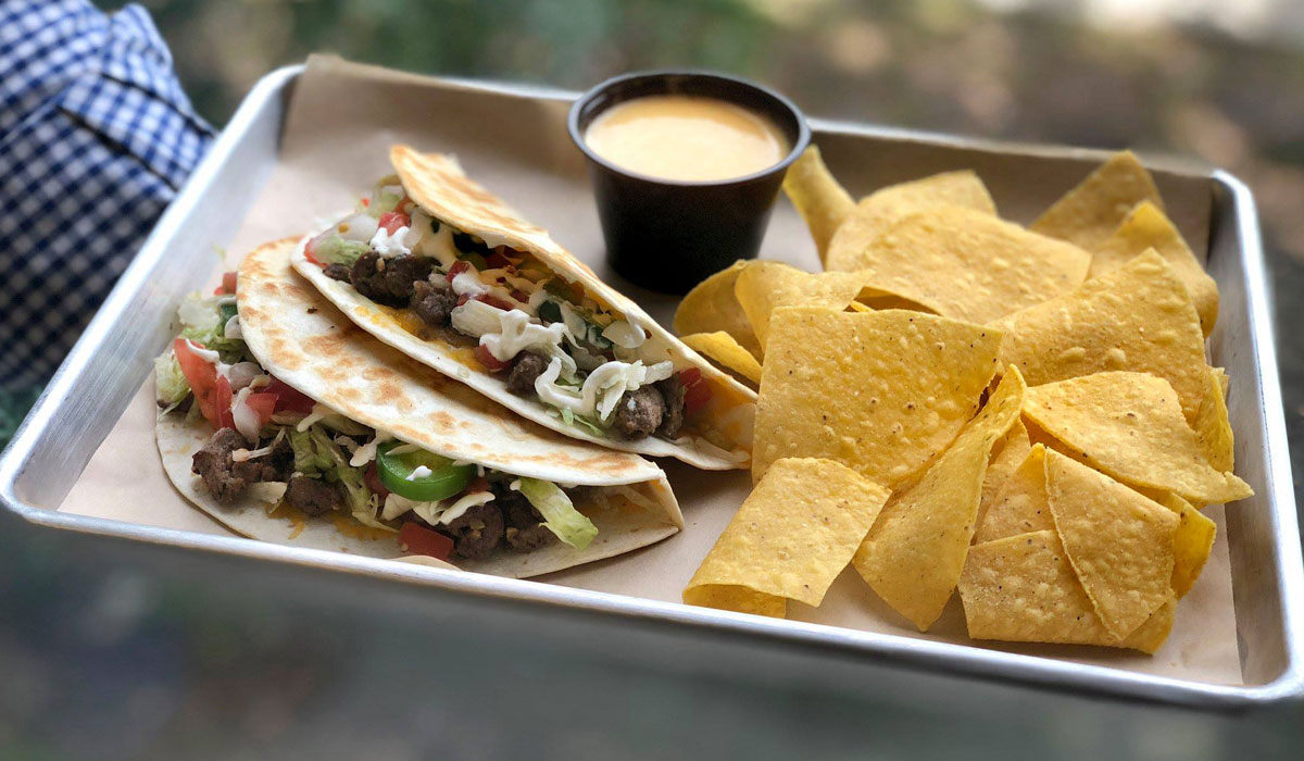 metal tray with tortilla chips nacho sauce and two beef tacos