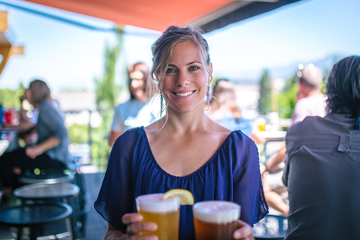 A waitress poses for a photo holding two freshly poured beers.