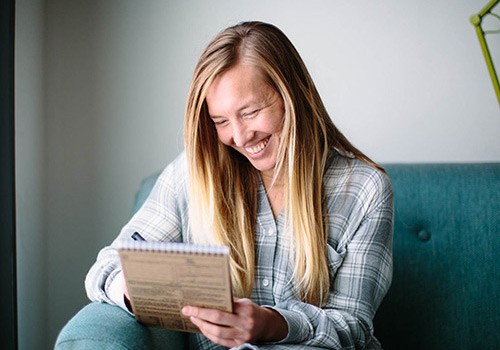 Wisetail LMS President, Ali Knapp, sits on a couch writing notes.