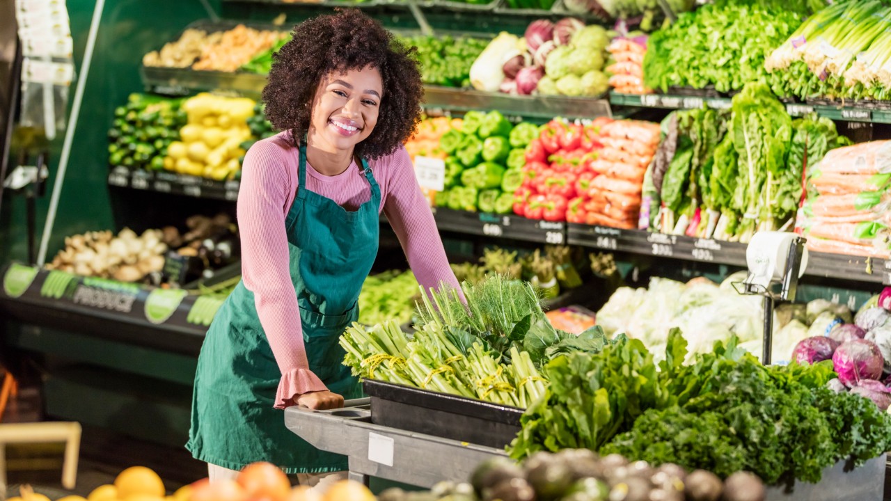 A food retail employee stocks vegetables at a grocery store.
