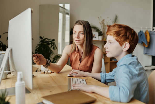A young boy works on the computer with his Mom while she teaches him.