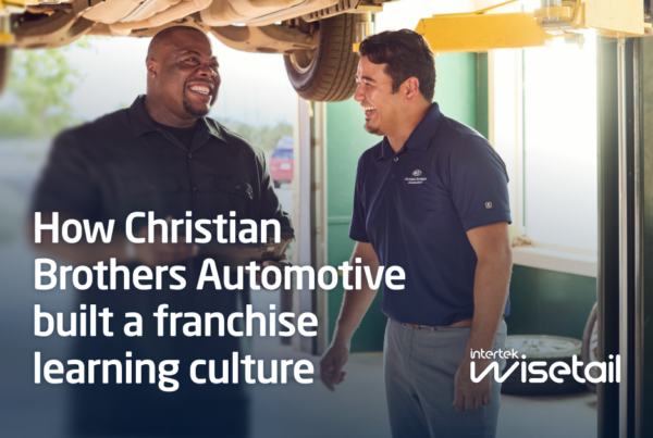 Two men smiling and talking in an auto repair shop. One is wearing a black shirt, and the other a blue polo. Text overlay discusses building a franchise learning culture.