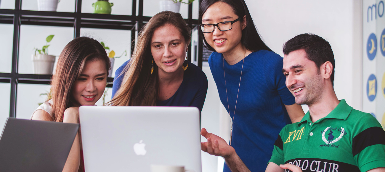 four coworkers gathered around a computer, pointing and engaged with each other