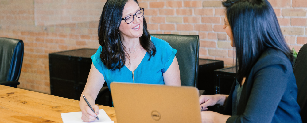 Two women conversing by an open laptop