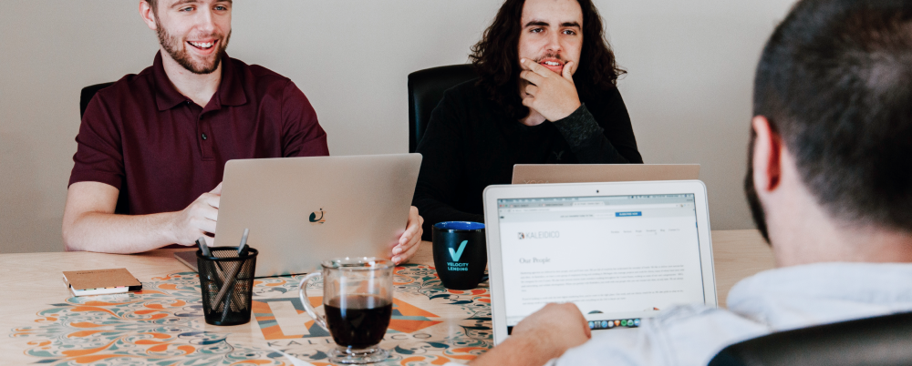 people using computers at a desk having conversation
