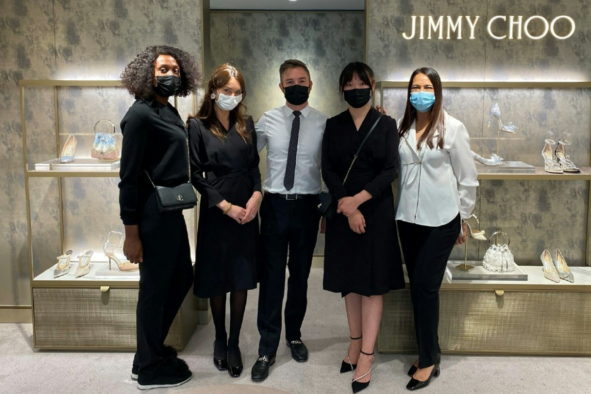 Capri Holdings team standing in front of Jimmy Choo brand label