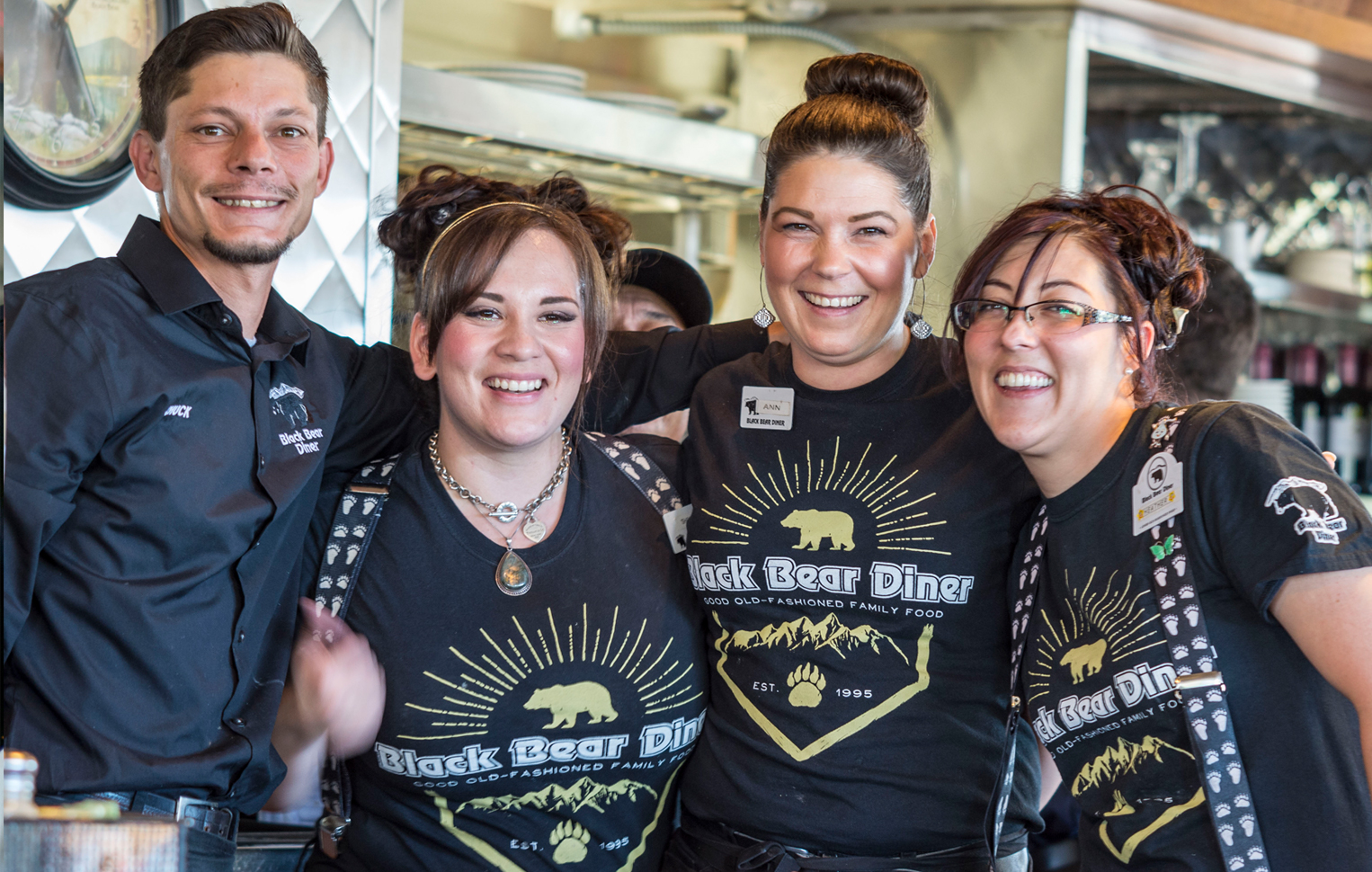 four happy people standing in a diner, wearing shirts that say Black Bear Diner