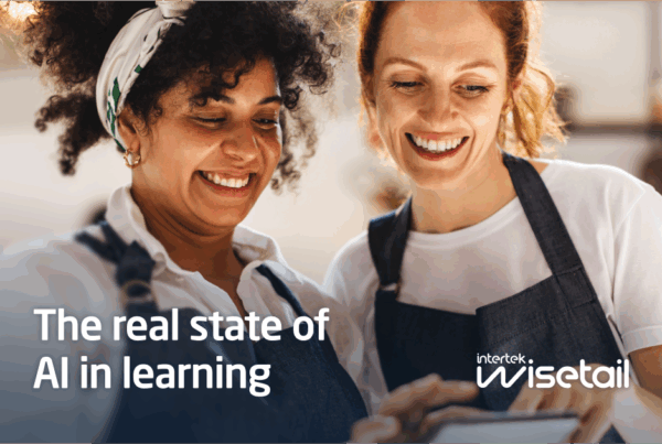 Two women who work at a restaurant smiling at an ipad, with the title "The real state of AI in learning" overlaid and the Wisetail logo in the bottom right.