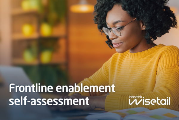 A woman in a yellow sweater and glasses works at a laptop in a warmly lit, cozy space. Text overlay reads "Frontline enablement self-assessment, Intertek wisetail."