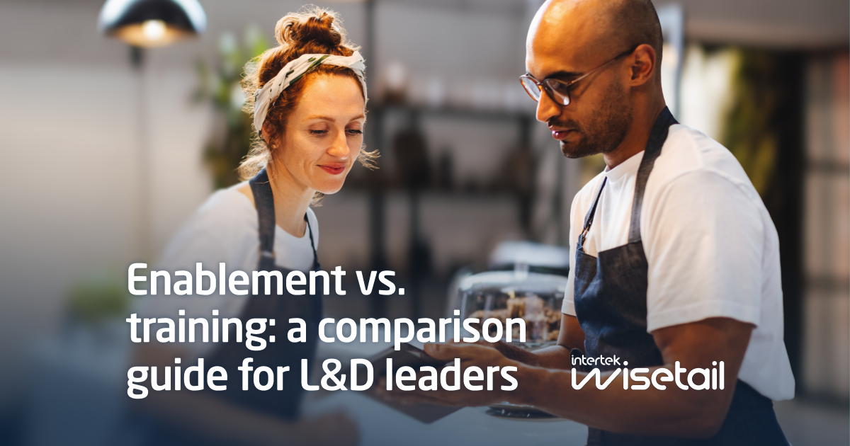 Two people in aprons are talking in a warmly lit, blurred kitchen setting. Text reads, "Enablement vs. training: a comparison guide for L&D leaders." Mood is collaborative.