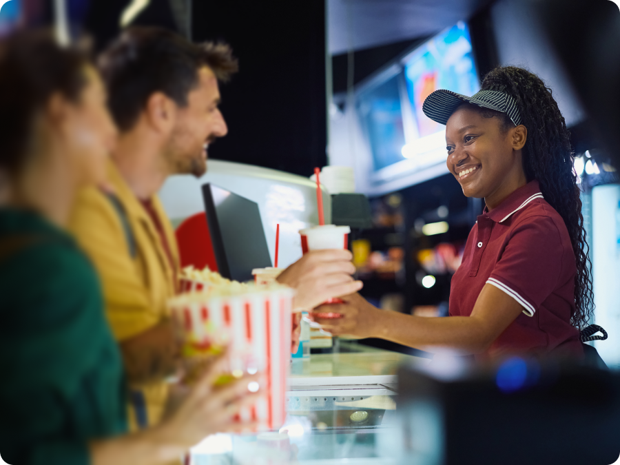 Frontline worker in a red polo handing drinks to customers at a concession counter.